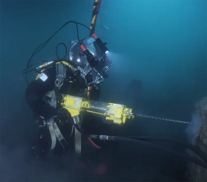 Commercial diver drilling underwater into concrete during subsea construction work